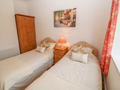 A bedroom with two single beds a wooden wardrobe a bedside table with a lamp and red floral curtains at Dirreen House Athea near Listowel County Kerry