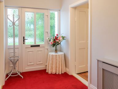 An entryway with a white door a white coat rack a small round table with a flower arrangement and red carpet at Dirreen House in Athea near Listowel County Kerry