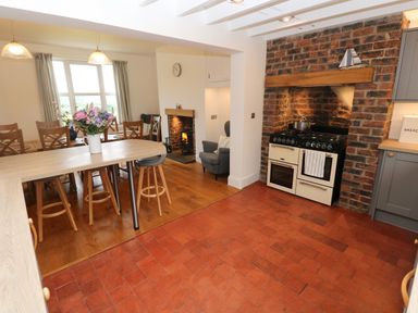 A kitchen and dining area with a brick fireplace stove wooden chairs a dining table with flowers and a small fireplace at Copybush Cottage in Lawrenny