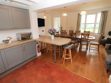 A kitchen and dining area with grey cabinets a microwave a wooden counter with stools and a dining table with chairs at Copybush Cottage in Lawrenny