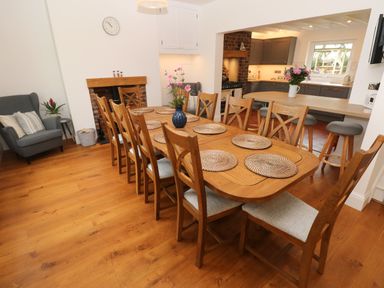 A dining room with a wooden table and chairs next to an open kitchen with a counter and stools at Copybush Cottage in Lawrenny