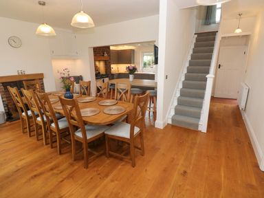 A dining room with a wooden dining table and chairs a staircase and a kitchen at Copybush Cottage in Lawrenny