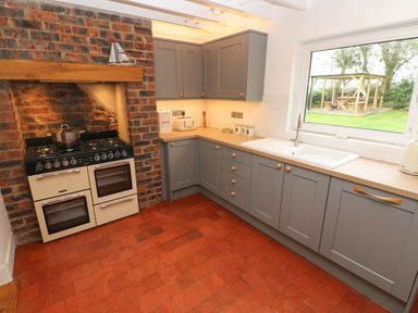 A kitchen with grey cabinets, a double oven stove, and a window showing an outdoor seating area at Copybush Cottage in Lawrenny