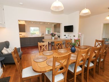 A dining room with a wooden table and chairs next to a kitchen with gray cabinets at Copybush Cottage in Lawrenny