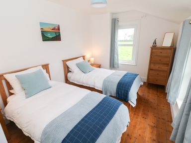 A bedroom with two single beds a wooden dresser and a window with curtains at Copybush Cottage in Lawrenny