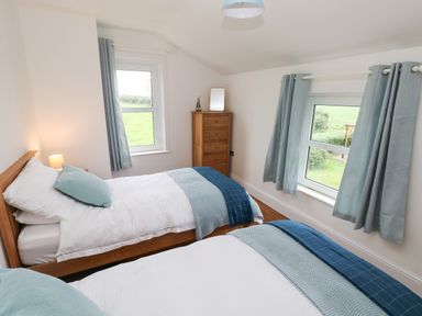 A bedroom with two single beds blue curtains and a wooden chest of drawers at Copybush Cottage in Lawrenny