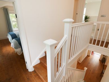 A wooden staircase with white railings leading to a hallway with doors and a bedroom visible at Copybush Cottage in Lawrenny