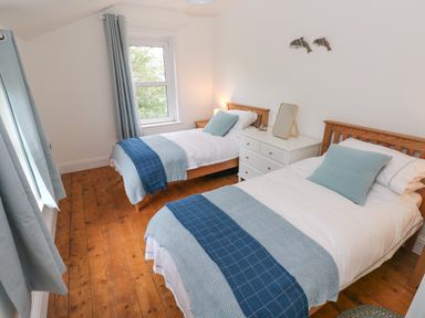 A bedroom with two single beds wooden floor and white walls at Copybush Cottage in Lawrenny