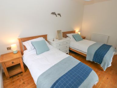 A bedroom with two single beds wooden bedside tables and a white dresser at Copybush Cottage in Lawrenny