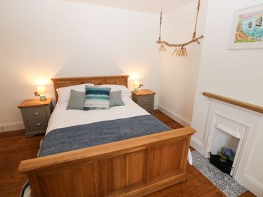 A bedroom with wooden bed and bedside tables with lamps a small fireplace and hanging branch with clothes hangers at Copybush Cottage in Lawrenny