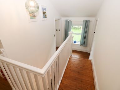 A hallway with wooden floor and white banister near a window with blue curtains at Copybush Cottage in Lawrenny