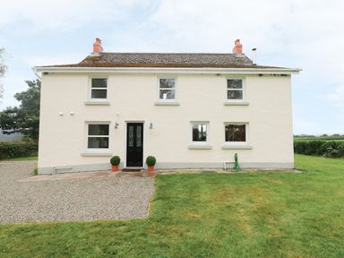 An exterior view of a two-story house with a black front door and multiple windows in a grassy and gravelled area at Copybush Cottage in Lawrenny