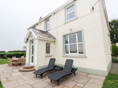 An outdoor patio area with two black lounge chairs a small table and a wooden dining table with chairs outside a two-story house at Copybush Cottage in Lawrenny