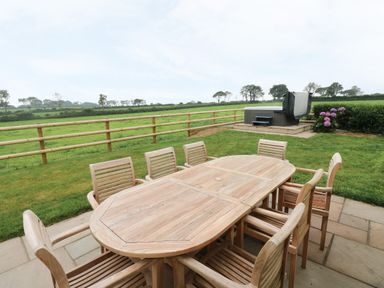 An outdoor seating area with a wooden table and chairs near a hot tub and a grassy field at Copybush Cottage in Lawrenny