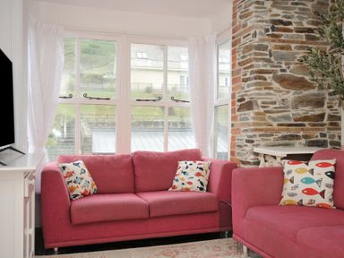 A living room with pink sofas and a television at Stargazy in Trebarwith Strand near Tintagel