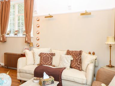 A living room with a cream sofa with pillows and curtains by a window at The Old School in Downham Market