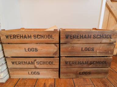 Two stacks of wooden crates labeled Wereham School Logs on a wooden floor next to a door at The Old School in Downham Market