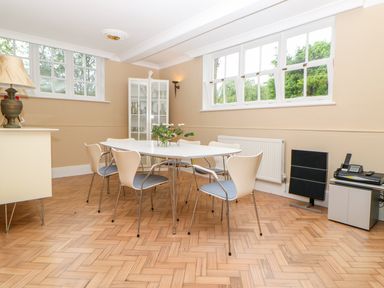 A dining room with a white table and six chairs wooden parquet flooring and large windows at The Old School in Downham Market