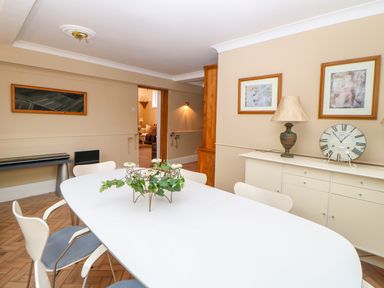 A dining room with a white table and chairs and a sideboard with a lamp and clock at The Old School in Downham Market