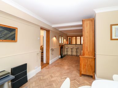 A dining area with white chairs and a table adjacent to a room with a wooden floor and bar stools at The Old School in Downham Market