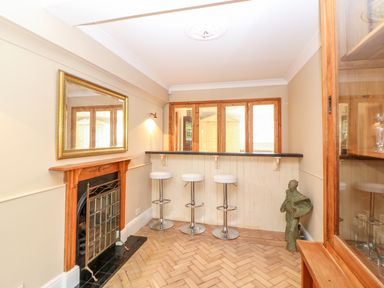A room with a fireplace a large mirror a bar counter with three stools and a small statue at The Old School in Downham Market
