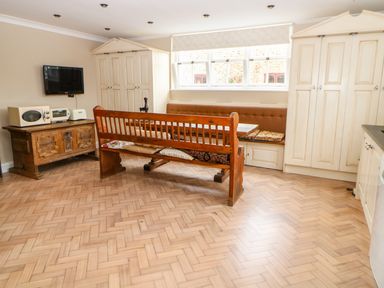 A kitchen with a wooden bench and table a television microwave and cupboards at The Old School in Downham Market