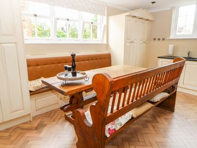 A kitchen dining area with a wooden table and benches by windows at The Old School in Downham Market
