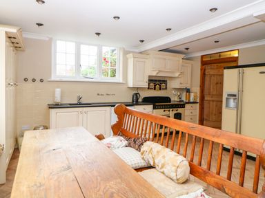 A kitchen with wooden dining bench cushions stove refrigerator and window at The Old School in Downham Market