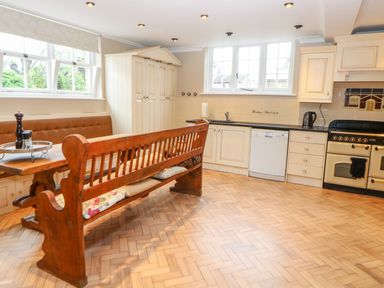 A kitchen with wooden bench seating a dining table and cream cabinets with large windows at The Old School in Downham Market