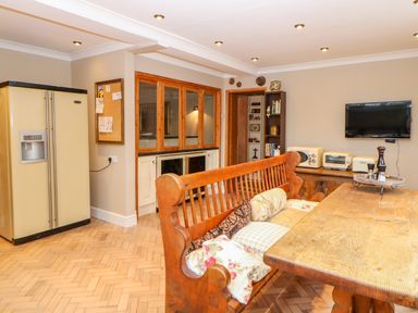 A kitchen with wooden bench seating around a wooden table and a cream refrigerator at The Old School in Downham Market