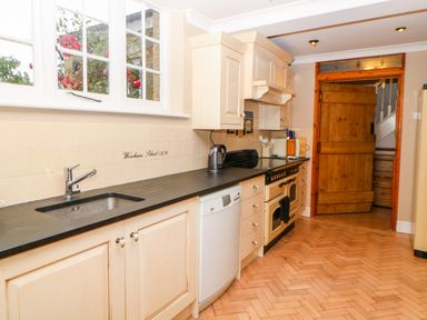 A kitchen with cream cabinets black countertop dishwasher and wooden door at The Old School in Downham Market