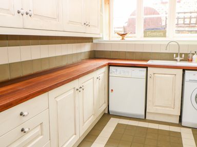 A kitchen with wooden countertops white cabinets a dishwasher under the counter and a window above the sink at The Old School in Downham Market