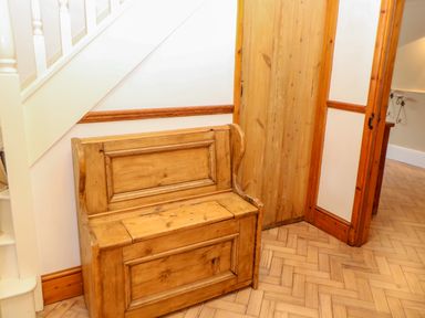 A wooden storage bench under a staircase next to a wooden door in a hallway at The Old School in Downham Market