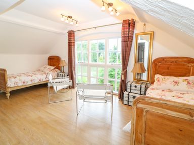 A bedroom with two wooden single beds floral bedding two metal framed chairs large window with curtains and a floor mirror at The Old School in Downham Market