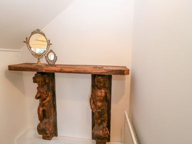 A wooden shelf supported by two carved cherub figures with two ornate mirrors on top at The Old School in Downham Market