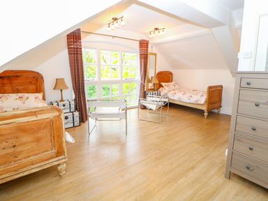 A bedroom with two wooden beds floral bedding two chairs a chest of drawers and a large window at The Old School in Downham Market