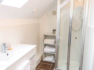 A bathroom with a sink cabinet a shelf with towels and a glass shower enclosure at The Old School in Downham Market