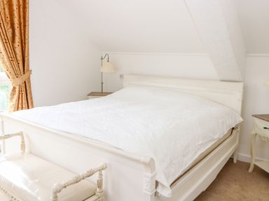 A bedroom with a white bed and a bench at the foot of the bed with orange curtains at The Old School in Downham Market