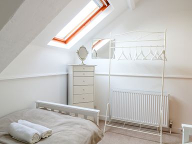 A bedroom with a bed and folded towels a chest of drawers with a mirror a clothes rack with hangers and a skylight window at The Old School in Downham Market