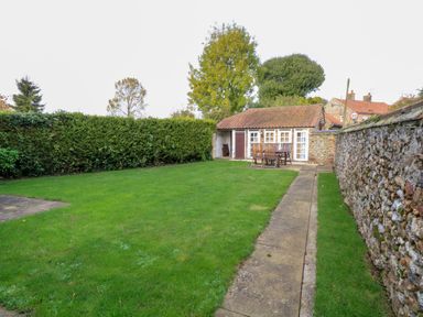 A garden with green lawn and patio furniture near a small outbuilding with tiled roof and stone wall at The Old School in Downham Market