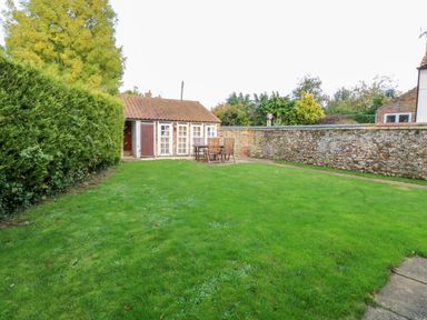 A garden with green grass wooden table and chairs near a small building with tiled roof and white doors at The Old School in Downham Market