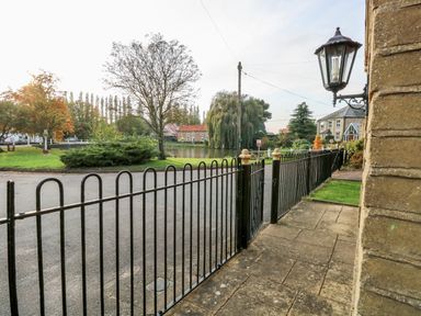 A fenced patio area with a lamp and a view of trees and houses across a road at The Old School in Downham Market