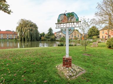 A village green with a pond and a sign reading wereham surrounded by houses and trees at The Old School in Downham Market