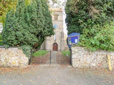 An old stone church with a clock tower behind a black metal gate and surrounded by trees at The Old School in Downham Market