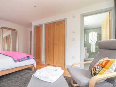 A bedroom with a bed and pink blanket grey armchair with a pillow and an en suite bathroom at Idlewild 2 Wheal Turnavore St Agnes