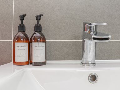 A bathroom sink with two amber pump bottles labeled hand lotion and hand wash next to a chrome faucet at Idlewild 2 Wheal Turnavore in St Agnes