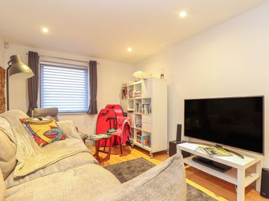 A living room with a beige sofa and colorful cushion a TV on a white stand a red chair and a white bookshelf at Idlewild 2 Wheal Turnavore in St Agnes