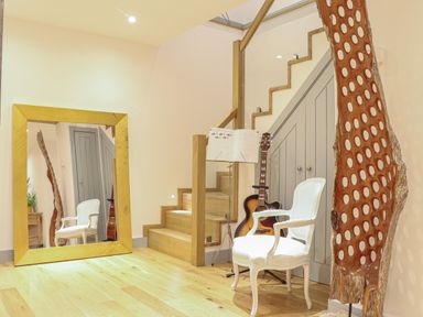 A wooden staircase with a white chair guitar and music stand beside a large mirror and wooden sculpture at Idlewild 2 Wheal Turnavore in St Agnes