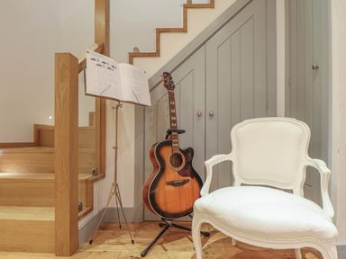 A guitar on a stand with a music stand and sheet music near wooden stairs and a white chair at Idlewild 2 Wheal Turnavore in St Agnes