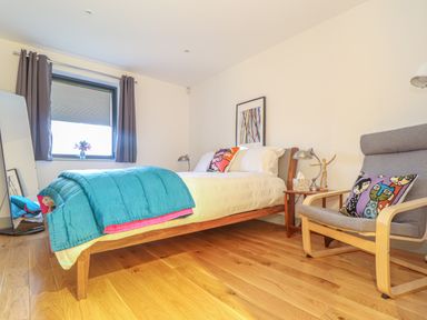 A bedroom with a bed a chair a window and wooden floor at Idlewild 2 Wheal Turnavore in St Agnes